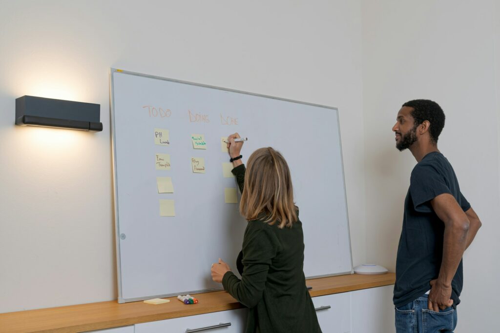 2. Two people collaborating and presenting ideas in front of a whiteboard covered with written content.